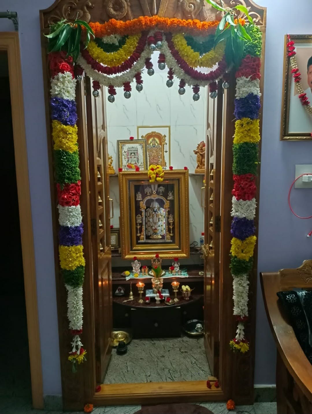 Pooja room doorway decorated with colourful garlands and mango leaves